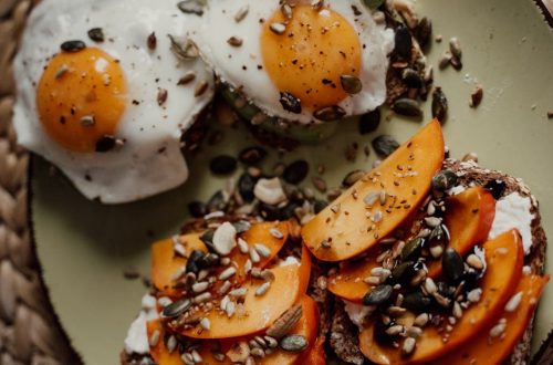 Delicious breakfast plate featuring avocado toast with fried eggs and persimmons, topped with seeds for a healthy start.